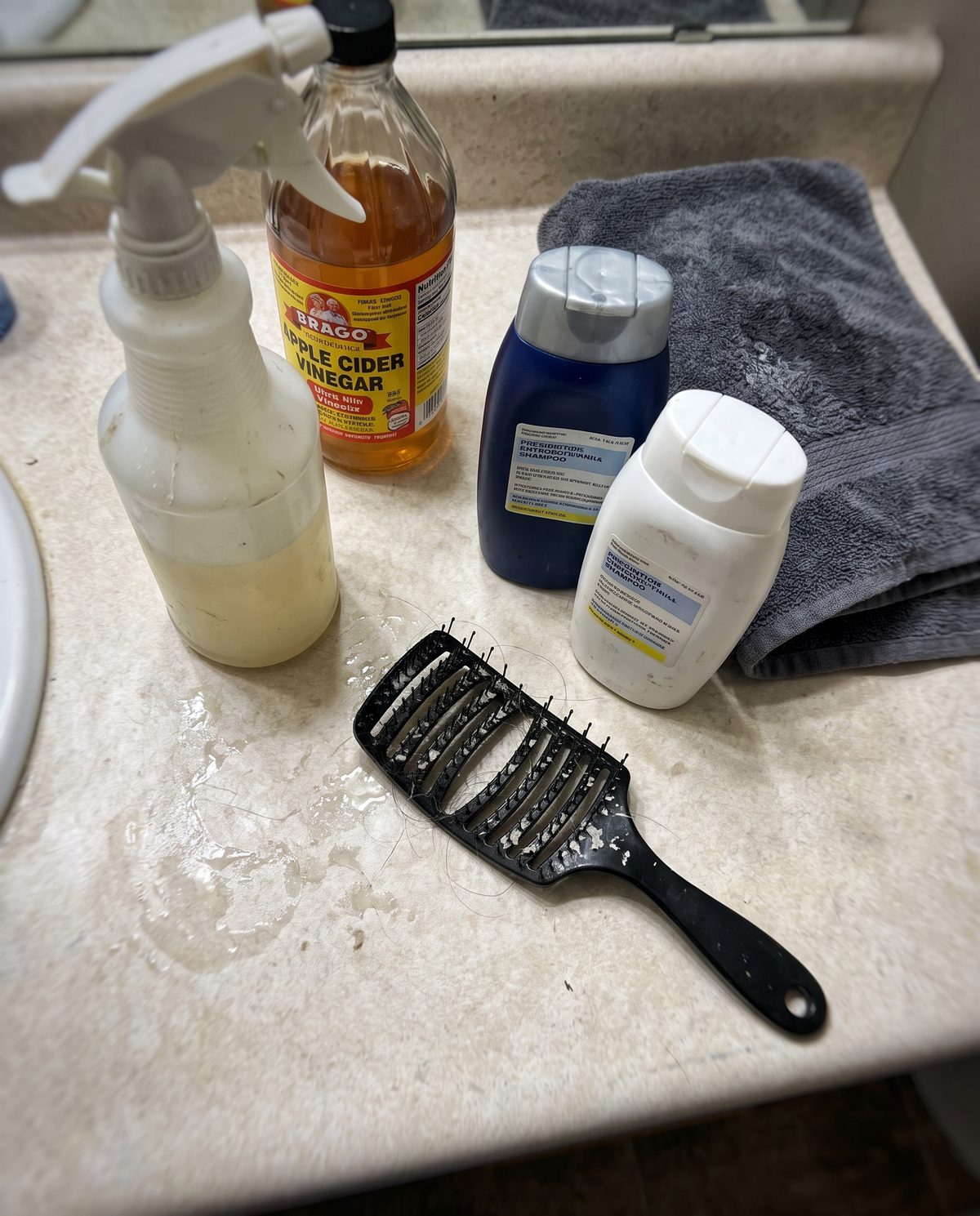 A bathroom counter with shampoo bottles, a spray bottle and a scalp brush